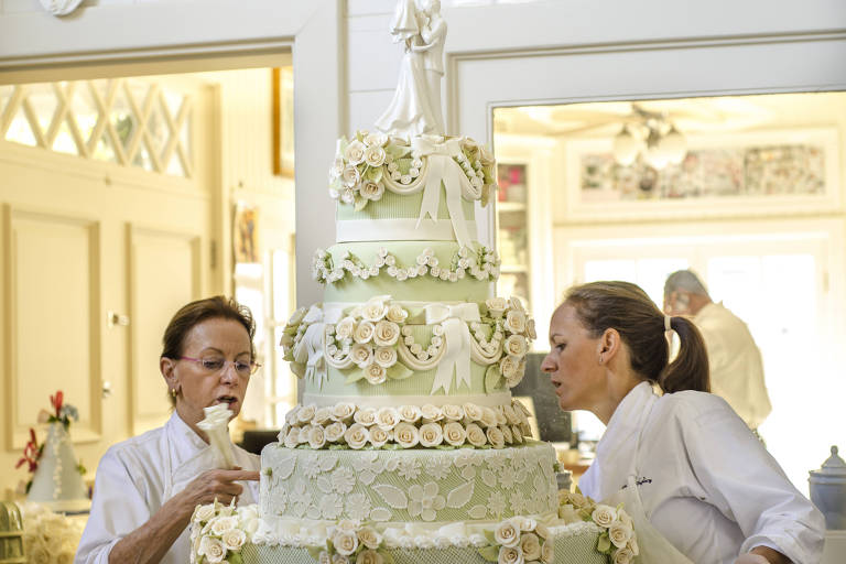 As duas mulheres trabalham decorando um bolo de casamento branco com flores
