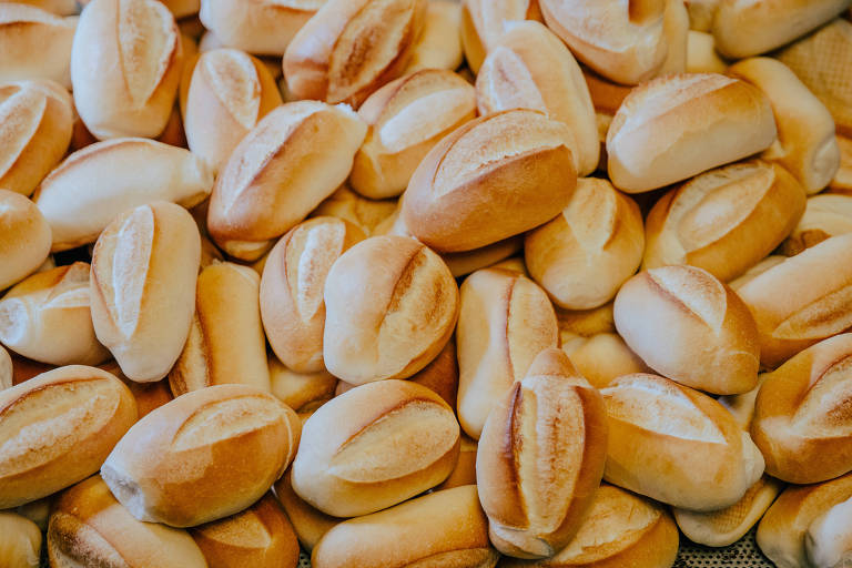 A imagem mostra uma grande quantidade de pães franceses, também conhecidos como pães de sal ou pães de trigo. Eles têm uma crosta dourada e crocante, com um corte característico no topo.
