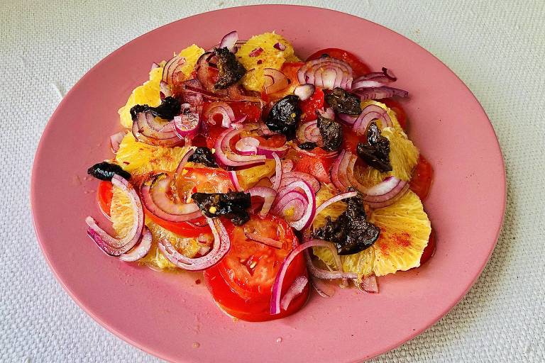 Em fundo branco, é visto um prato cor-de-rosa com uma salada composta por tomate e abacaxi