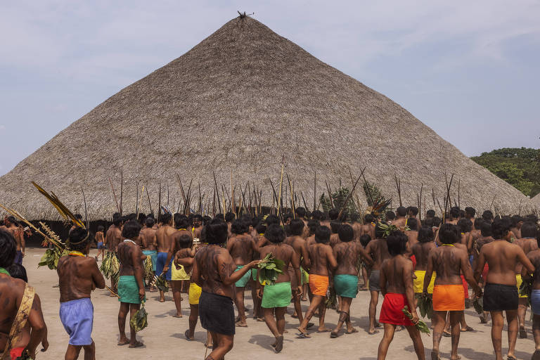 foto mostra indígenas durante cerimônia, estão todos de costas, voltados para uma grande tenda ao fundo 