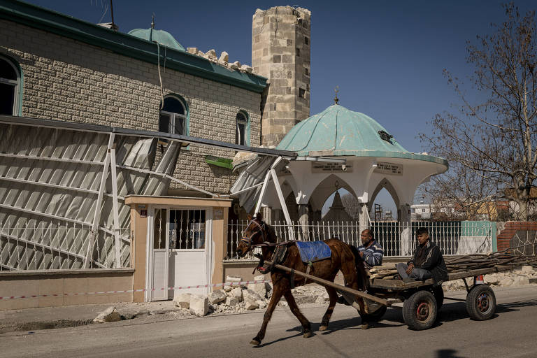 Homens passam em frente a mesquita danificada por terremoto na cidade de Erzin, na Turquia