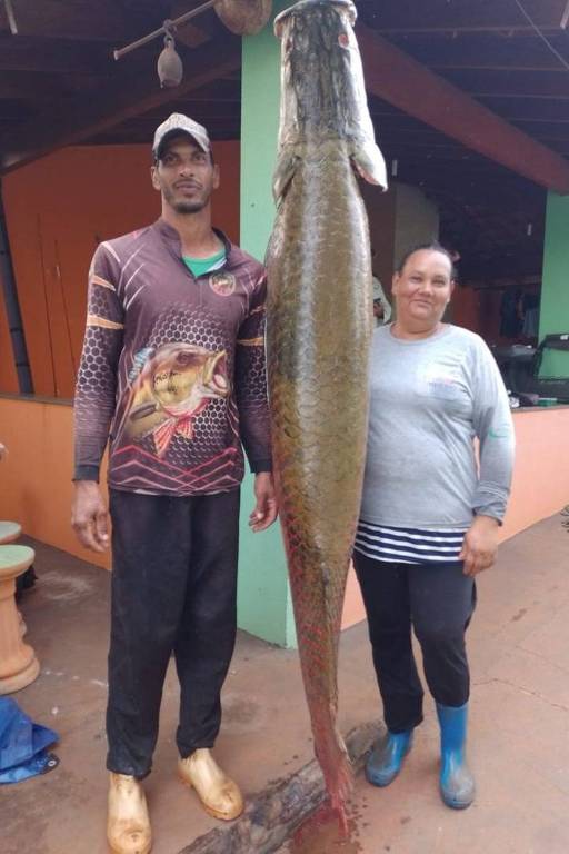 Um casal posa ao lado de um grande peixe pendurado