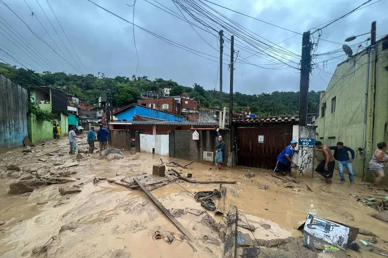 Moradores e casas cercados por água barrenta que encobre rua