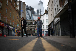 FILE PHOTO: People walk past shops, with the City of London financial district in the background, in London, Britain