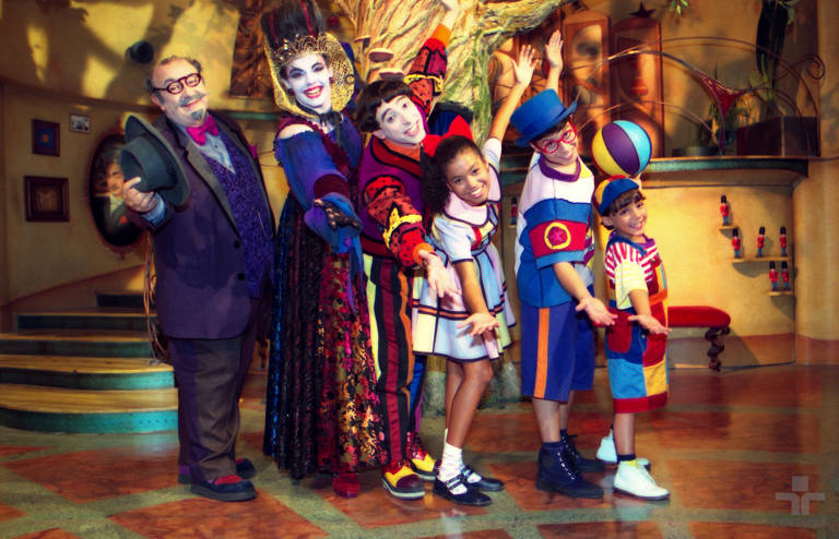 três atores adultos e três crianças posam para foto caracterizados como os personagens da serie infantil dentro do estudio