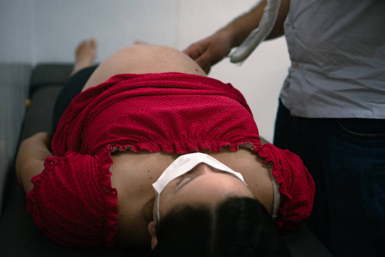 Gestante com blusa vermelha, usando máscara de proteção, é examinada por médico de família em Unidade Básica de Saúde da Ilha do Combu, em Belém (PA) 