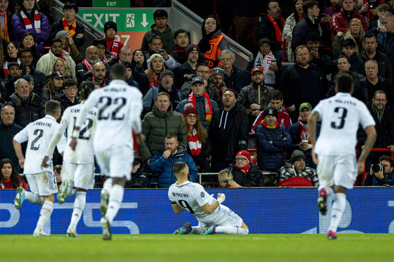Observado por colegas de Real Madrid, Benzema ajoelha-se no estádio Anfield para festejar gol no 5 a 2 do seu time no Liverpool, nas oitavas de final da Liga dos Campeões da Europa