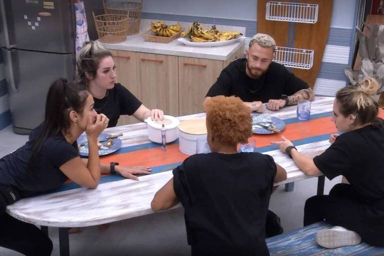 Em foto colorida, grupo conversa em torno de uma mesa da cozinha