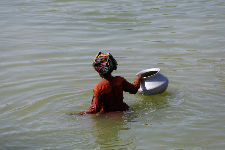 Mulher passa por área inundada do Paquistão, que sofreu com as chuvas de monções em 2022