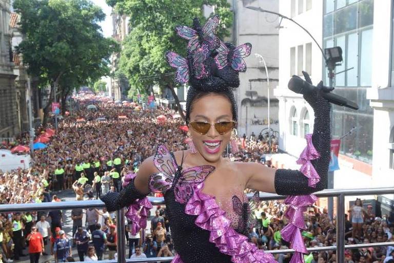 Anitta com roupa inspirada em Carmen Miranda, no alto do trio elétrico; uma multidão ao fundo