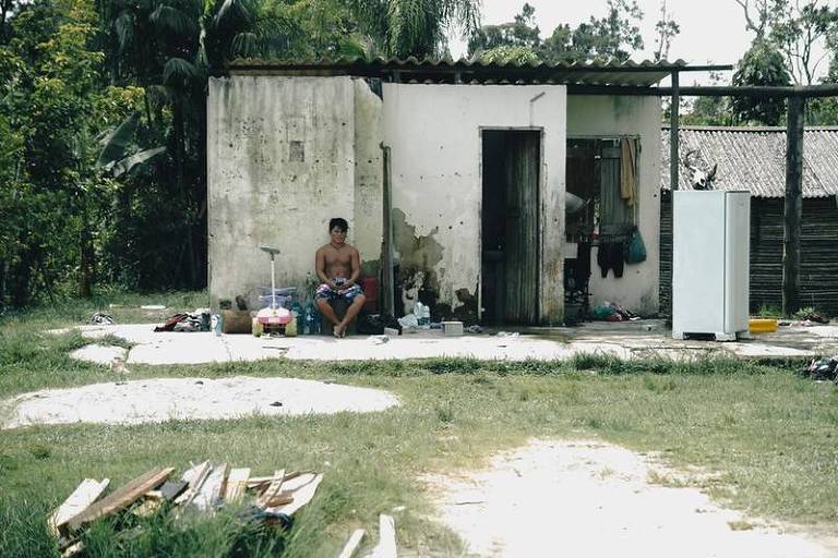 Indígena é visto sentado do lado de fora de casa em aldeia
