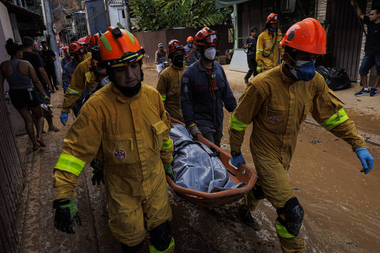 Socorristas, usando roupas amarelas e capacetes alaranjados, carregam corpo coberto por saco plástico, retirado dos escombros em São Sebastião, no litoral norte de São Paulo