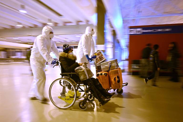 Trabalhadores com roupas de proteção ajudam cidadã da China que chega em aeroporto de Roma, na Itália