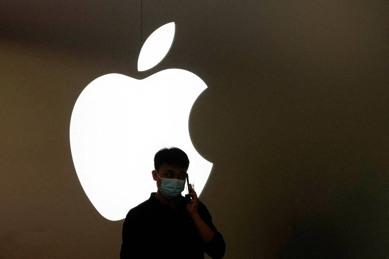 Homem fala em iPhone em frente a logo da Apple, em loja da empresa em Shangai
