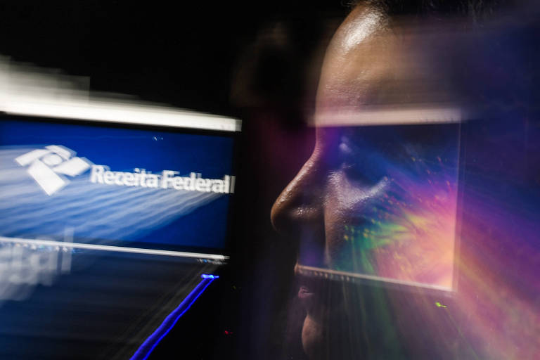 Imagem colorida mostra Tânia, de perfil, olhando para a esquerda, com o reflexo da luz do monitor do computador ao fundo