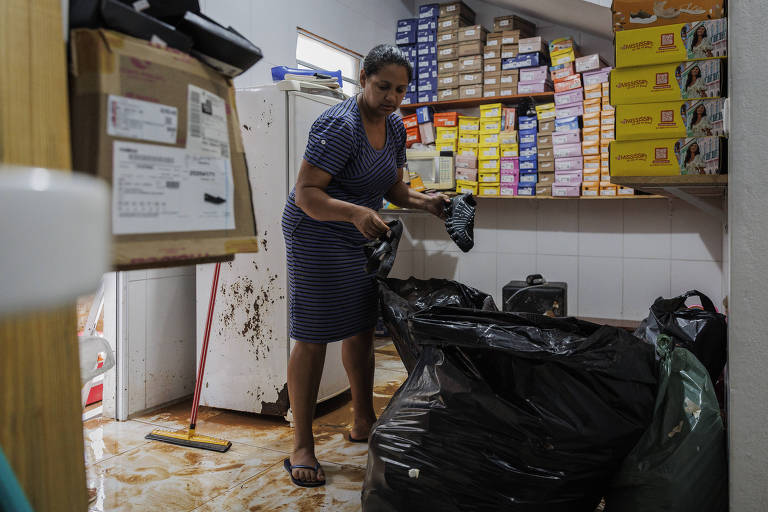 A comerciante Rosana Ribeiro Soares recolhe os pares de sapatos destruídos pela enchente em sua loja; ela calcula seu prejuízo em mais de R$ 80 mil