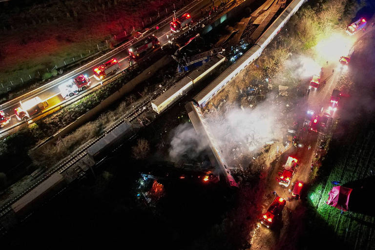 a foto aérea, tirada à noite, mostra os vagões dos trens que colidiram descarrilados, alguns ao chão. o acidente é rodeado por carros e outros veículos de socorristas