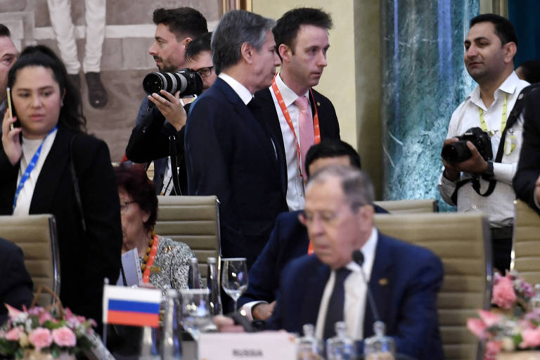 Blinken, ao centro, acompanhado por um homem de gravata rosa, passa por Lavrov, sentado, na reunião de chanceleres do G20 em Nova Déli