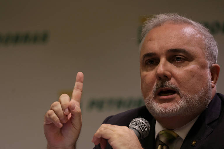 Foto mostra o presidente da Petrobras, Jean Paul Prates, homem branco com cabelo e barba grisalhos que está usando terno, falando com um microfone na mão esquerda e o indicador levantado na mão direita
