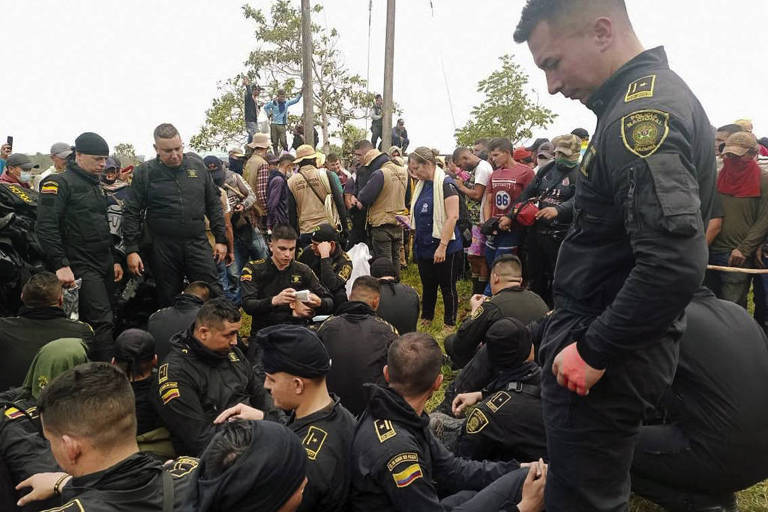 Imagem mostra grupo de policiais sentados de preto no chão, reféns de manifestantes