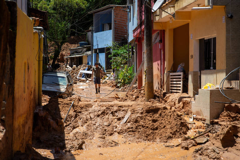 Rua cheia de lama alaranjada é cercada por casas e carros cobertos pelo barro