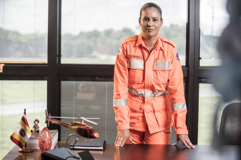 A foto mostra a nova chefe do Estado-Maior do corpo de bombeiros de Minas Gerais, coronel Daniela Lopes Rocha da Costa, de 47 anos, com roupa da corporação atrás de sua mesa em sala da Cidade Administrativa, a sede do governo de Minas Gerais.