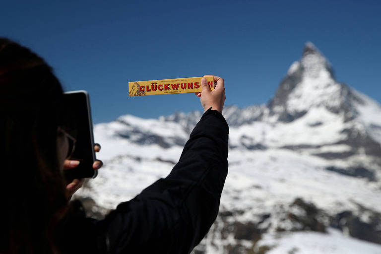 Turista fotografa o monte Matterhorn, na Suíça, com tablete de Toblerone em primeiro plano