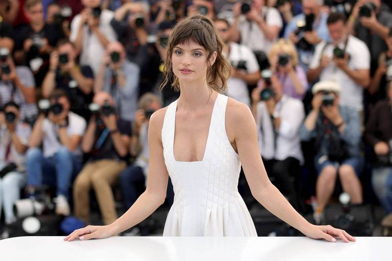 Mulher de vestido branco e cabelos presos posa no tapete vermelho do Festival de Cannes
