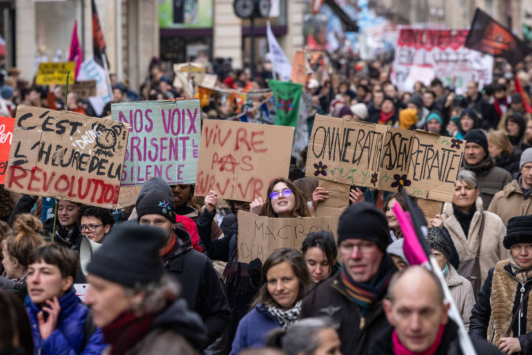 a foto mostra uma rua tomada por centenas de manifestantes, que carregam cartazes com dizeres em francês contra a reforma previdenciária