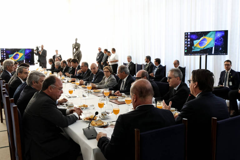 Bolsonaro e ministros sentados em volta de uma mesa retangular