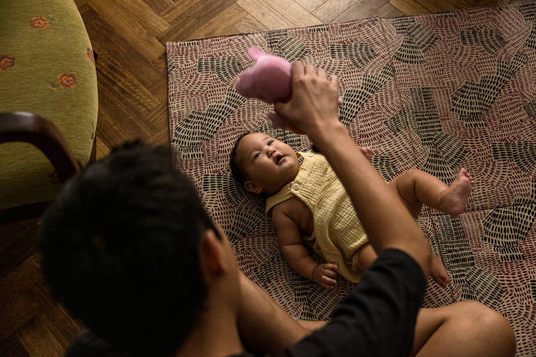 Homem mostra brinquedo para bebê deitado no chão