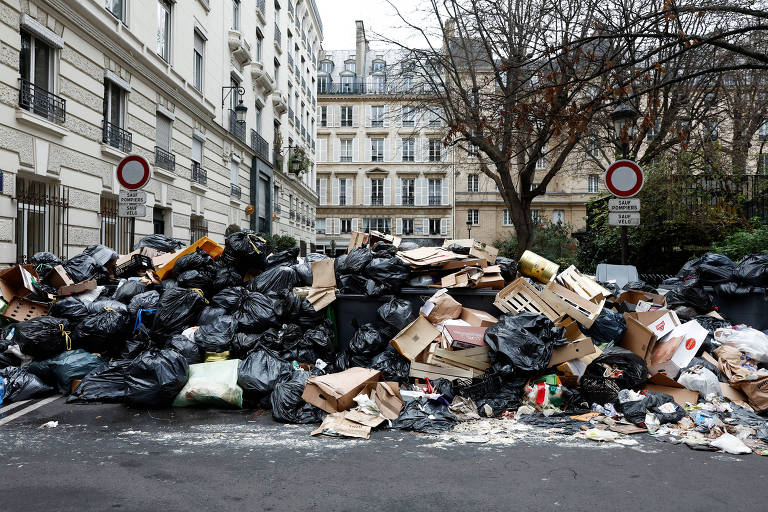 pilhas de lixo estão acumuladas numa rua de Paris. em segundo plano, estão os prédios característicos da capital francesa
