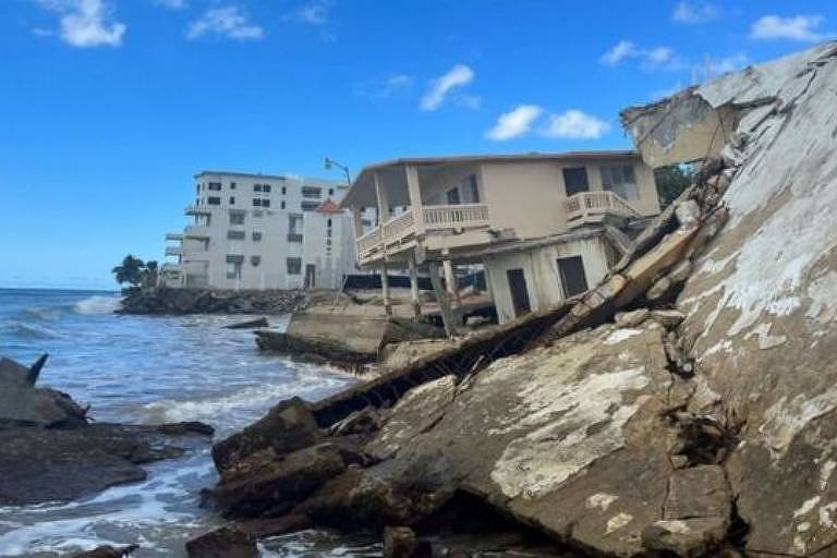 a fotografia mostra uma fileira de grandes casas destruídas pela ação do mar, tombando sobre a costa