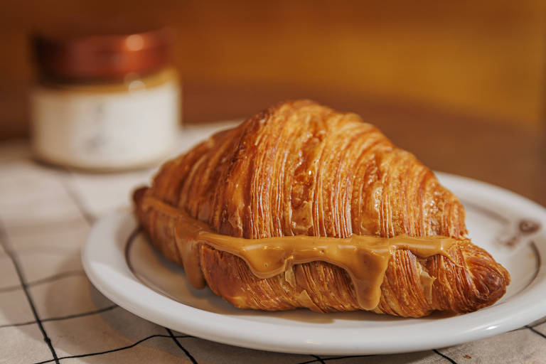 Croissant em um prato branco deixa escorrer um recheio amarronzado, a pasta de amendoim 
