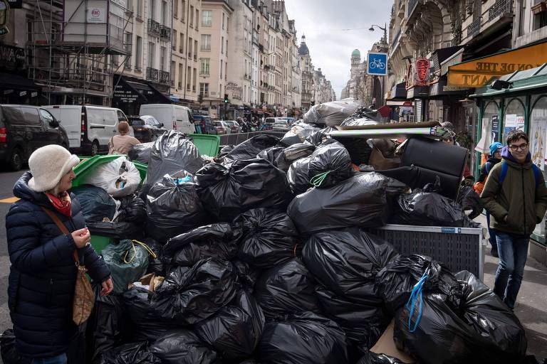 Pedestres andam em meio ao lixo que se acumula na calçada, reflexo da greve dos agentes de limpeza de Paris
