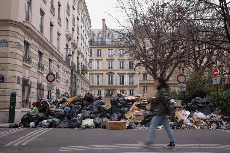 Pedestres andam em meio ao lixo que se acumula na calçada, reflexo da greve dos agentes de limpeza de Paris