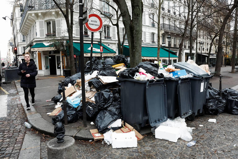 Pedestres andam em meio ao lixo que se acumula na calçada, reflexo da greve dos agentes de limpeza de Paris