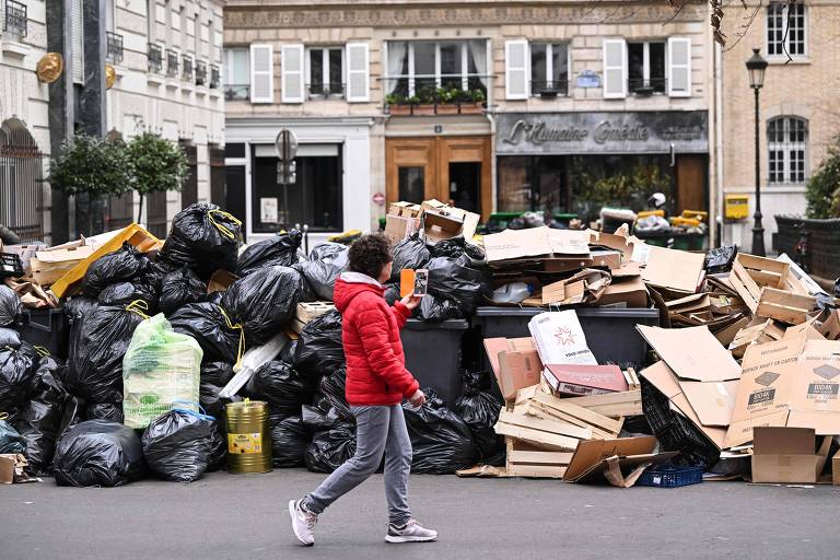 Pedestres andam em meio ao lixo que se acumula na calçada, reflexo da greve dos agentes de limpeza de Paris