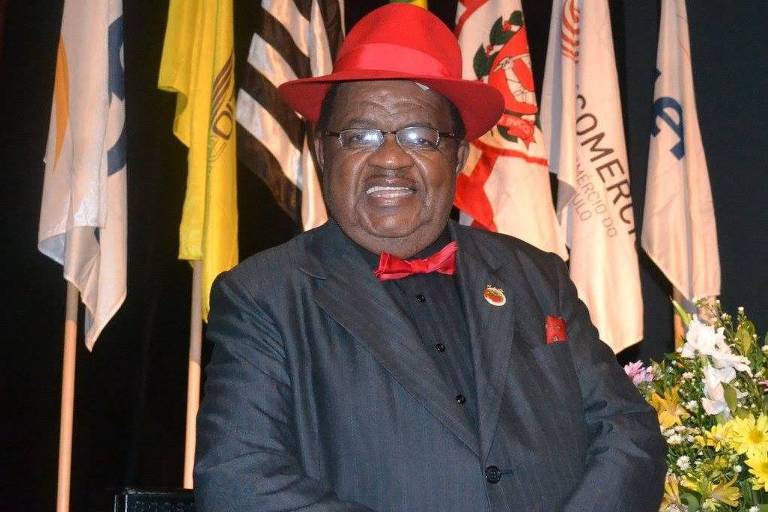 Homem negro com terno preto e chapéu vermelho