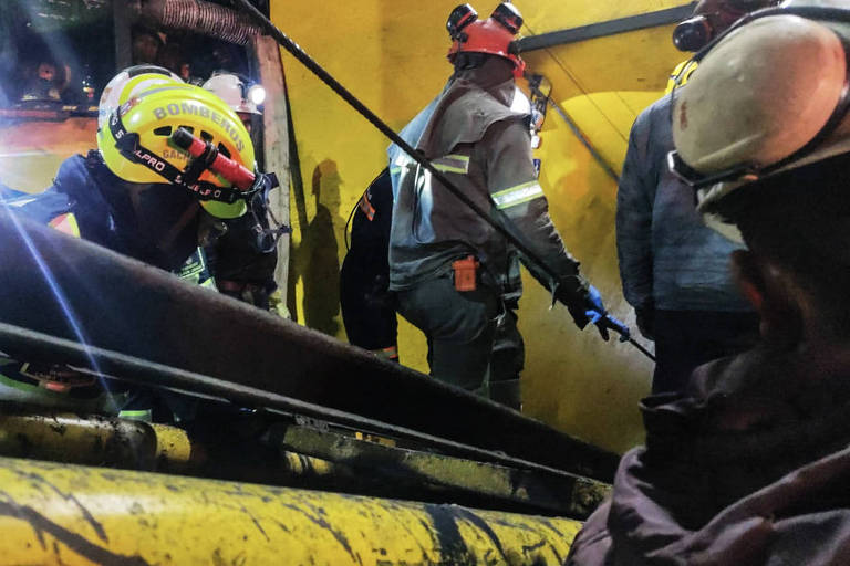 a foto mostra bombeiros devidamente paramentados usando uma máquina amarela no resgate aos mineiros soterrados