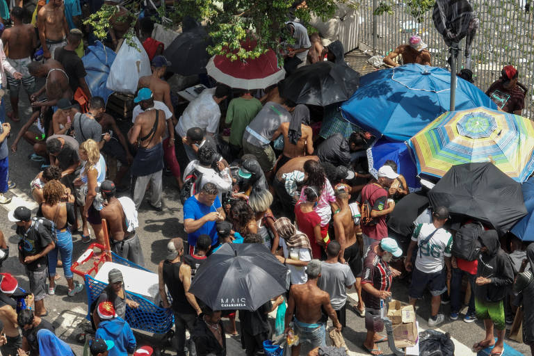 Diversas pessoas aglomeradas em uma trecho da rua, parte delas sob barracas armadas na calçada