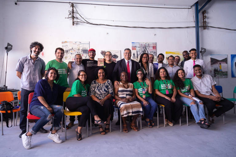 Ministro Flávio Dino visita ong no Complexo da Maré, zona norte do Rio de Janeiro. Na foto há jovens sentados, outro em pé. O ministro de terno no meio do grupo.