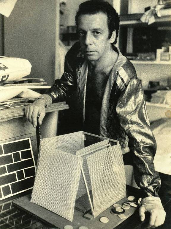 O artista brasileiro Hélio Oiticica diante de uma caixa, em seu estúdio, encarando a lente da câmera