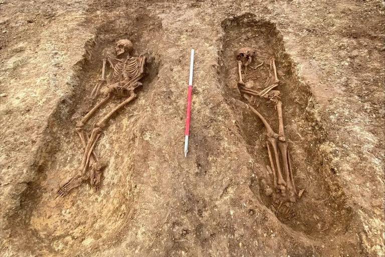 a foto mostra duas sepulturas cavadas no meio da terra, lado a lado, com dois esqueletos dentro