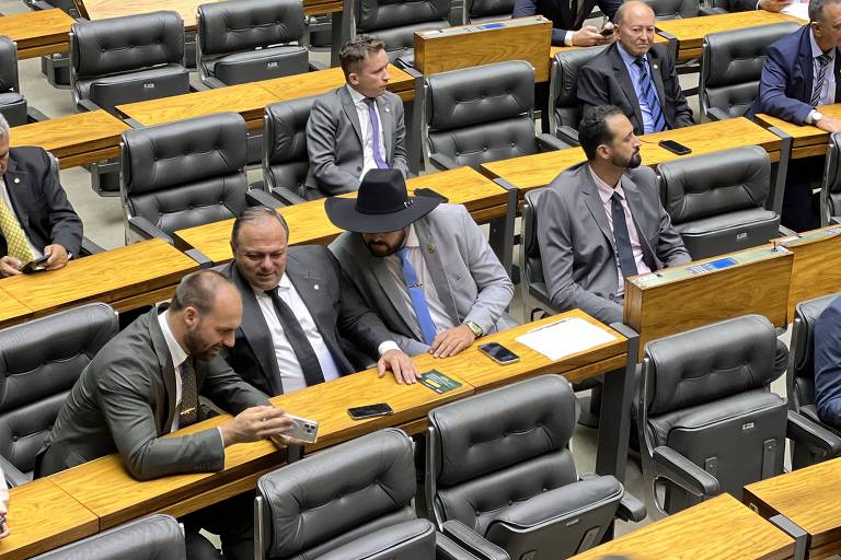 Deputados federais sentados no plenário da Câmara; Eduardo Bolsonaro mostra a Pazuello e Zé Trovão um vídeo em seu aparelho celular