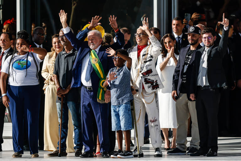fotografia colorida mostra o presidente Lula na rampa do Planalto, cercado por representantes de grupos como crianças, negros, indígenas, mulheres e pessoas com deficiência. eles estão com os braços erguidos, cumprimentando o público 