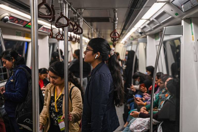 a foto foi tirada dentro de um metrô. no centro dela, em destaque, está uma jovem indiana de perfil. ela amarra seu longo cabelo num rabo de cavalo. diversas outras mulheres estão no vagão