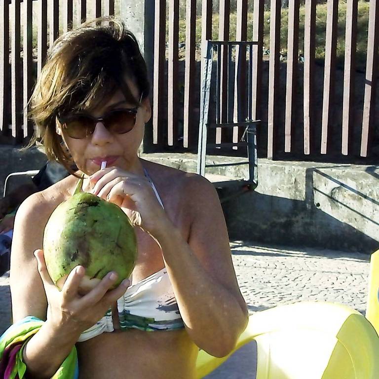 Mirian Goldenberg toma água de coco na praia
