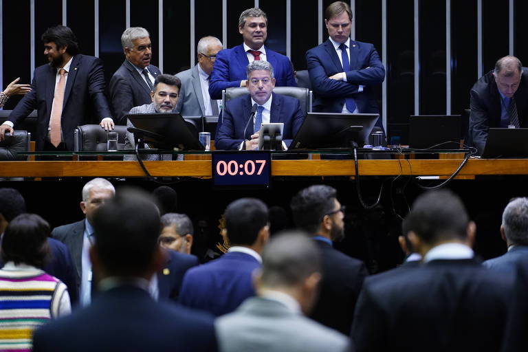Foto mostra mesa diretora da Câmara rodeada de parlamentares, com o deputado sentado ao centro