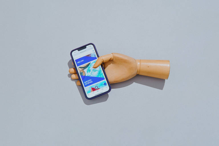 Mão segura celular com o aplicativo do Imposto de Renda na tela